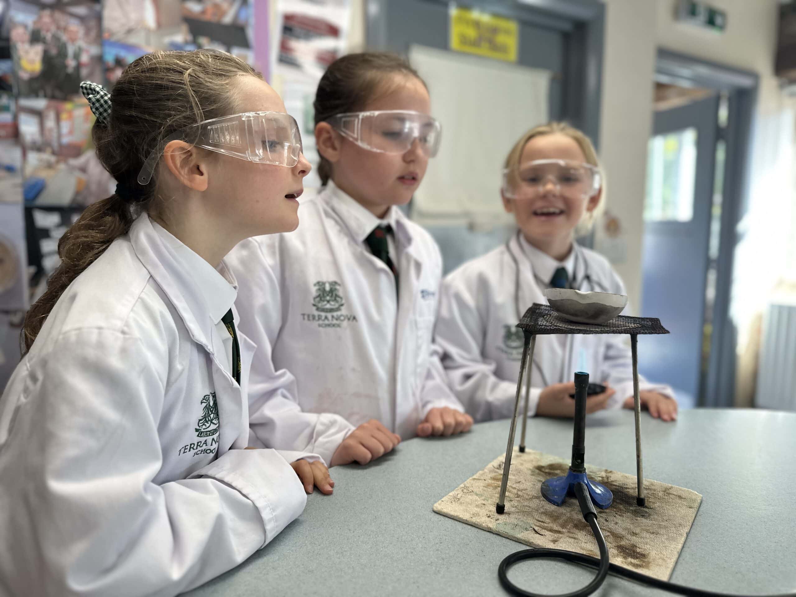 Three girls in science lab coats looking excited about experiment