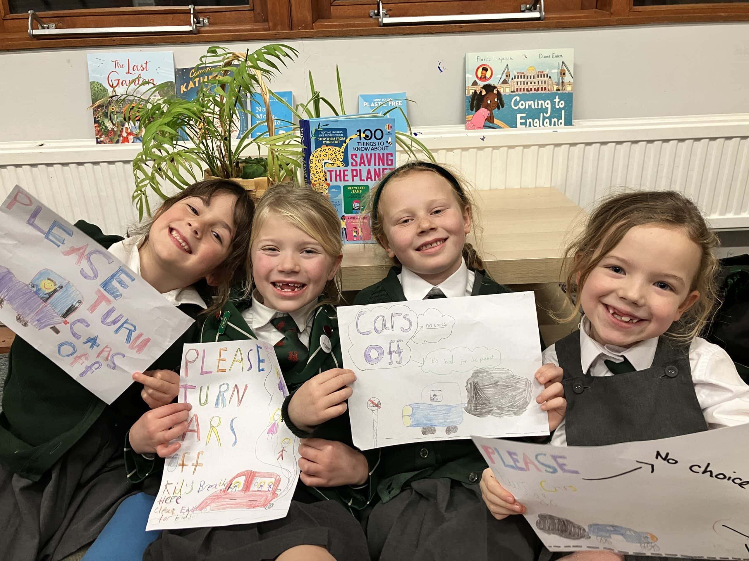 Four pupils holding posters encouraging parents to turn their car engines off when waiting