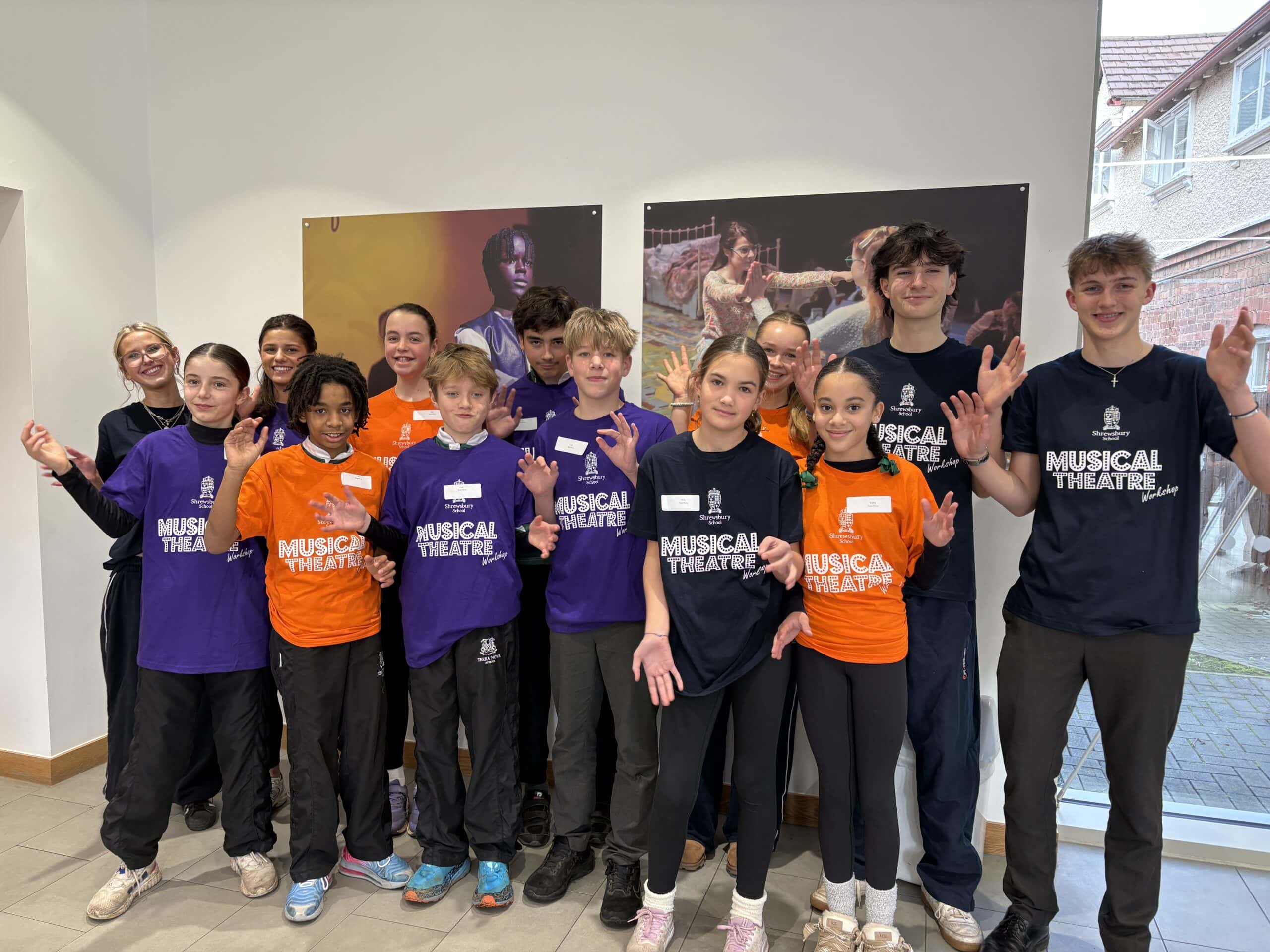 Children in brightly coloured t-shirts, in drama studio, doing jazz hands
